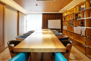Une salle de conférence avec une longue table, des chaises, un tableau blanc et une bibliothèque.