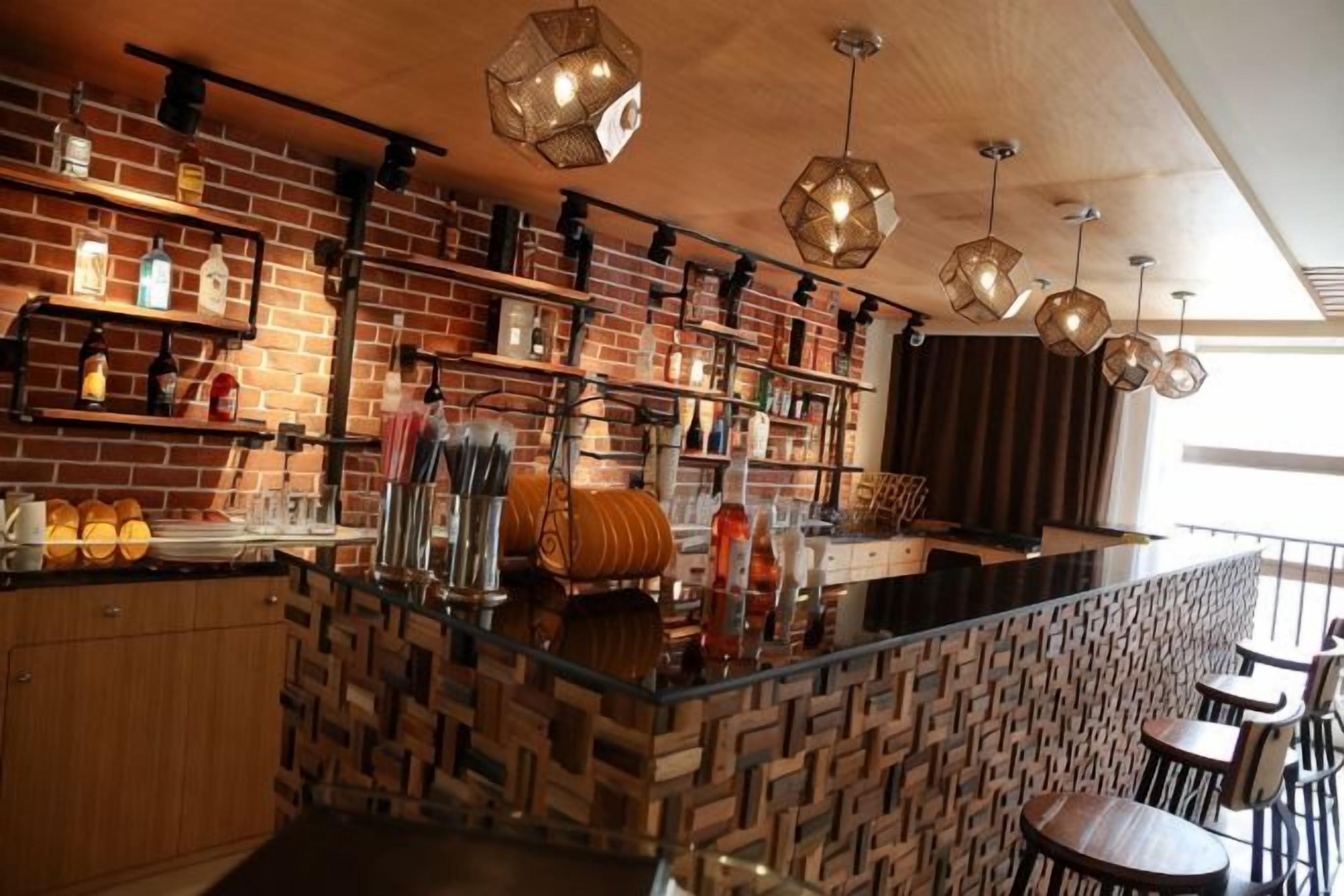 Un espace bar avec un mur en briques, des étagères remplies de bouteilles et des luminaires suspendus.