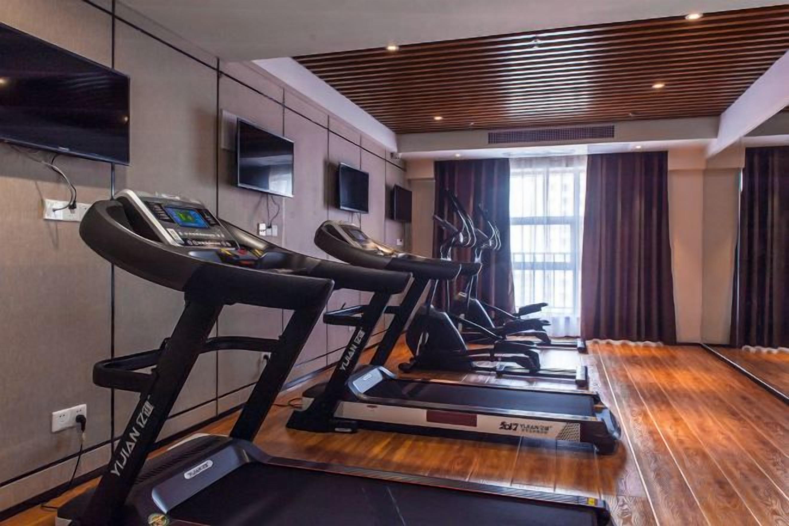 Une salle de sport équipée de tapis de course, d’un panneau de contrôle et d’une grande fenêtre avec des rideaux.