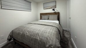 A bedroom with a bed, a window with blinds, a wall-mounted picture, and a door. - New suite in a great location. Central for shopping, restaurants and commuting. (Regina)