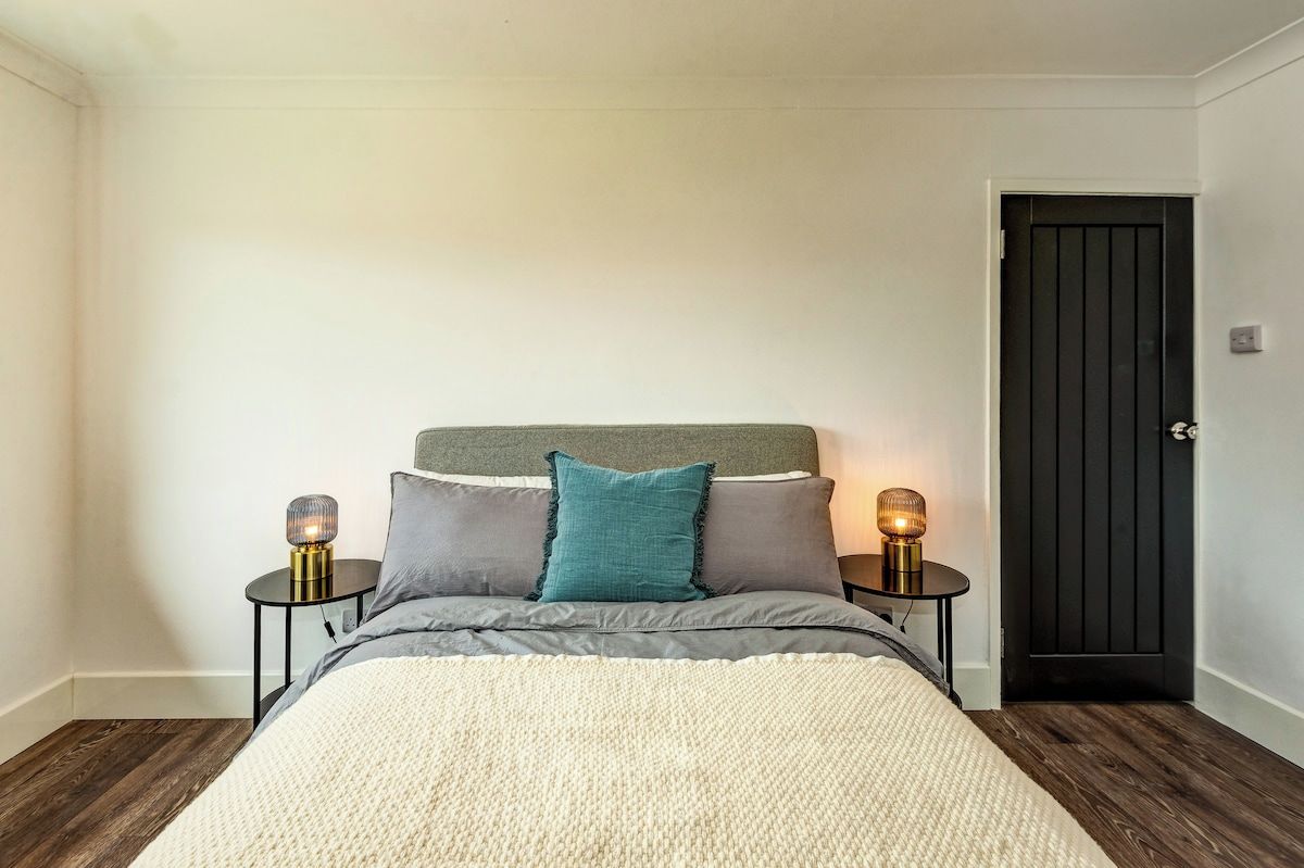 A bedroom with a bed, two bedside tables with lamps, a door, and a wooden floor.