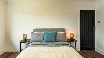 A bedroom with a bed, two bedside tables with lamps, a door, and a wooden floor.