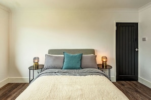 A bedroom with a bed, two bedside tables with lamps, a door, and a wooden floor. - 3-Bed Gosport Home | Ideal for Work (gosport)
