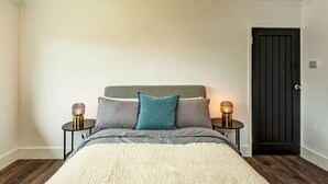 A bedroom with a bed, two bedside tables with lamps, a dark door, and wooden flooring.
