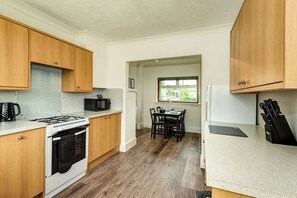 Cocina compacta con armarios de madera, estufa a gas, microondas y comedor con mesa y sillas.