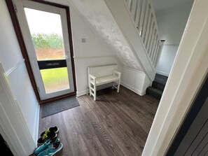 Una habitación con piso de madera, un banco blanco, un radiador y una puerta que da al exterior.