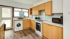 A compact kitchen with wooden cabinets, a washing machine, a stove, and a microwave.