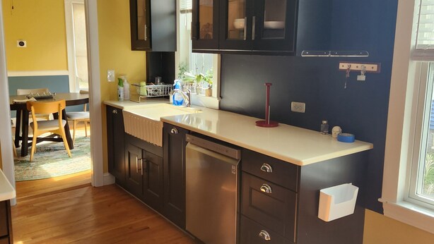 A kitchen with dark cabinets, a white countertop, and wooden flooring. - Coastal Charm  – Walk to Beach or Train! (Swampscott)