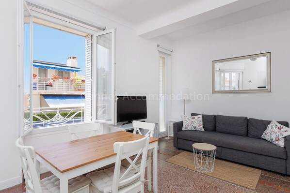 A modern living room with a grey sofa, a wooden dining table, and a TV.