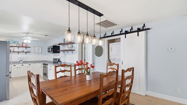 A modern kitchen with white cabinets, a wooden dining table, and hanging pendant lights. - Tybee Beach Cottage, Steps from all the local fun and a quick walk to the beach (Tybee Island)