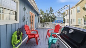 A deck with red and turquoise chairs, a barbecue grill, and a hose. - Tybee Beach Cottage, Steps from all the local fun and a quick walk to the beach (Tybee Island)