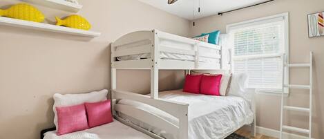 Quarto com beliche, ventoinha no teto, janela com persianas e prateleira com objetos decorativos.