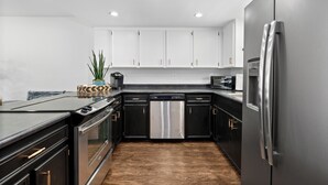 A modern kitchen with stainless steel appliances, black cabinetry, and a wooden floor.