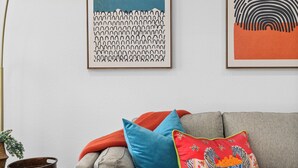 A living room with a grey sofa, colorful cushions, a blue side table, and two abstract paintings on the wall.