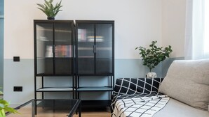 Un salon moderne avec un canapé, une table basse en verre, une étagère noire et une plante en pot.