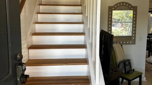Eine Treppe mit Holzboden und weißen Geländern, die zu einem Zimmer mit Fenster und Stuhl führt.