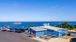 Un parc de caravanes a la costa, amb edificis blaus, taules de picnic i vistes a l'oceà.