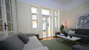 A living room with a grey sofa, a coffee table, and a grey armchair. There is a large window with a view of the outside.