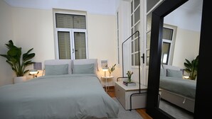 A bedroom with a bed, bedside tables, a mirror, and a window with shutters.