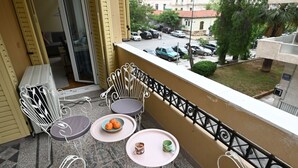 A balcony with white metal chairs and a small table, a bowl of fruit, and a cup on the table.
