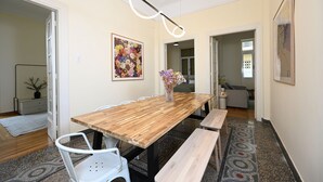 A dining area with a wooden table, white chairs, and benches. There is a vase with flowers on the table.