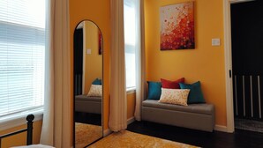 A hotel room with a bed, a sofa, a mirror, and a painting on the wall. - Cozy 3-Bedroom Home, Great Location in Downtown Huntingdon (Huntingdon)