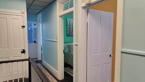 A hallway with white doors, a staircase with a patterned railing, and a green wall with a circular artwork. - Cozy 3-Bedroom Home, Great Location in Downtown Huntingdon (Huntingdon)