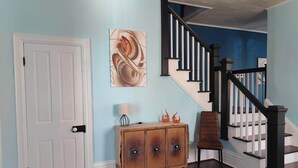 A hallway with a wooden door, a cabinet with decorative panels, a staircase with black railings, and a blue wall. - Cozy 3-Bedroom Home, Great Location in Downtown Huntingdon (Huntingdon)