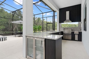 Cocina moderna con una isla grande, electrodomésticos integrados y un cerramiento de vidrio que ofrece vistas al exterior.