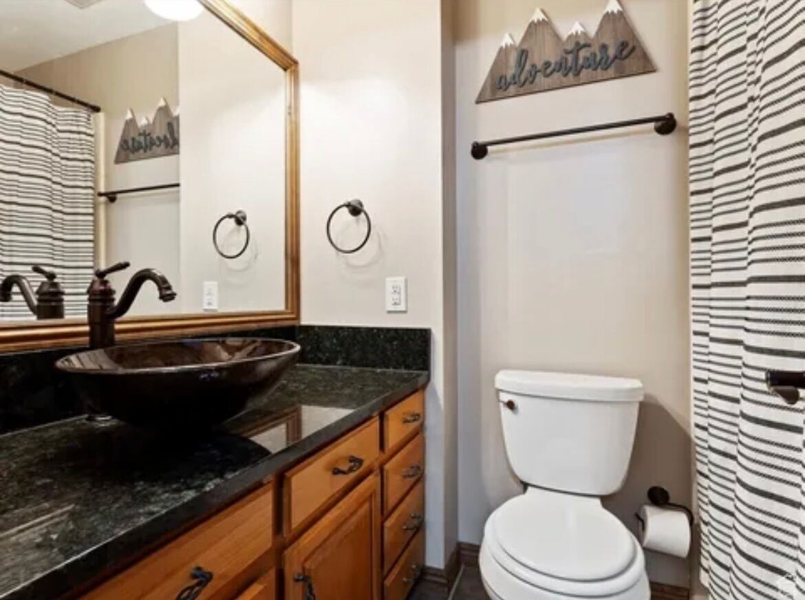 Une salle de bain avec un lavabo sur pied noir, des meubles en bois, des toilettes blanches et un porte-serviettes.