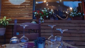 A restaurant with a wooden exterior, a large illuminated sign, and a table set with wine glasses and flowers. - L'Ostu Di San Giacu (Boves)