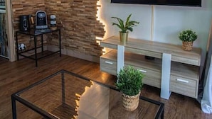 A modern living room with a wooden accent wall, a flat-screen TV, a coffee machine, and a glass coffee table. - Luxury apartment, swimming pool, tennis, beach (Cannes)