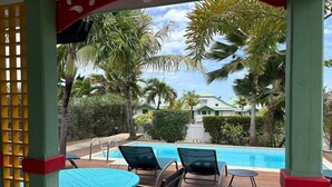 A pool area with wooden deck, lounge chairs, and a view of a building with a green roof. - Villa Koray, Orient Bay, pool , central location (Marigot)