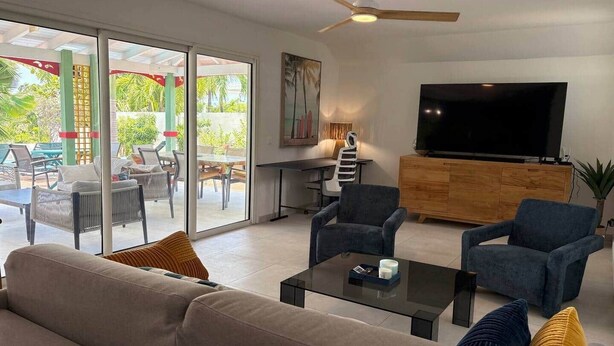 A living room with a sofa, armchairs, a coffee table, a TV, and a ceiling fan. - Villa Koray, Orient Bay, pool , central location (Marigot)