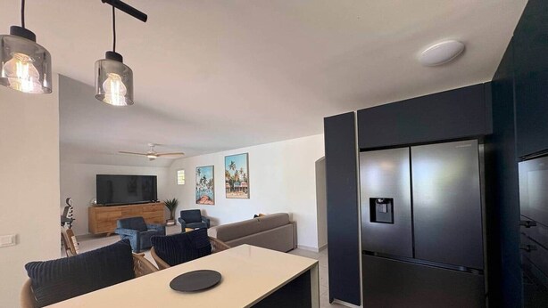 Eine moderne Küche mit integriertem Kühlschrank, ein Essbereich mit Tisch und Stühlen sowie ein Wohnzimmer mit Sofa und Fernseher.