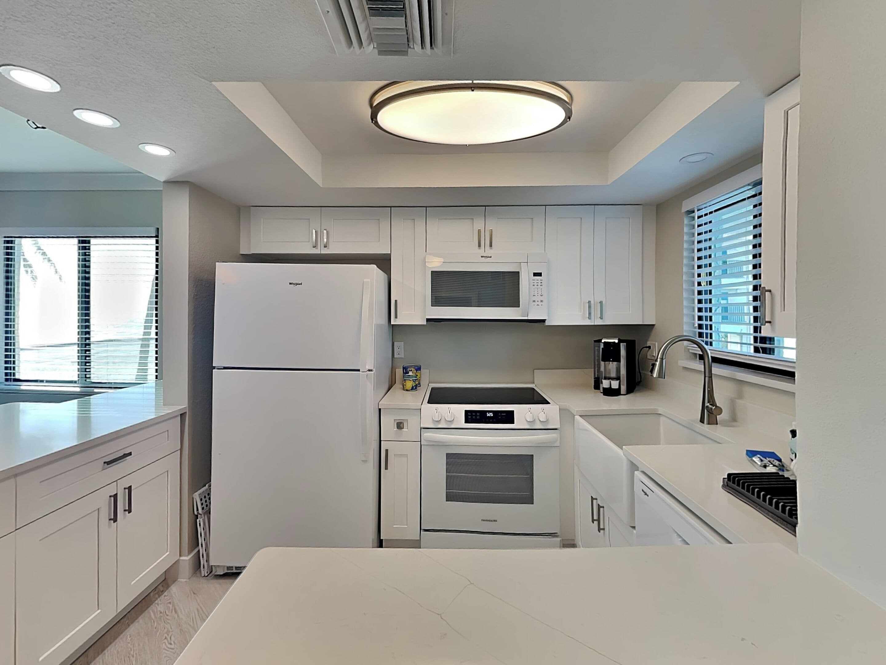 A modern kitchen with white cabinets, a built-in microwave, a refrigerator, a stove, and a sink.