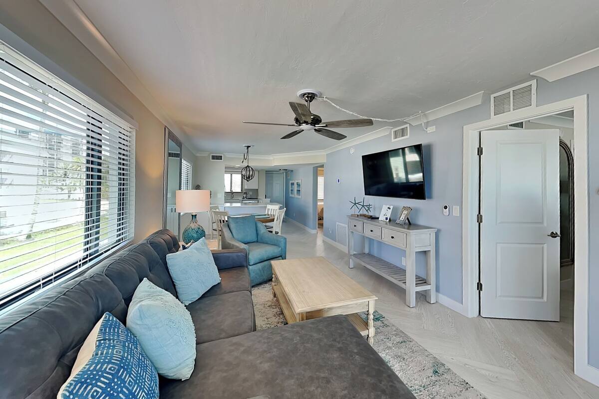 A modern living room with a grey sofa, blue cushions, a coffee table, and a TV on a stand.