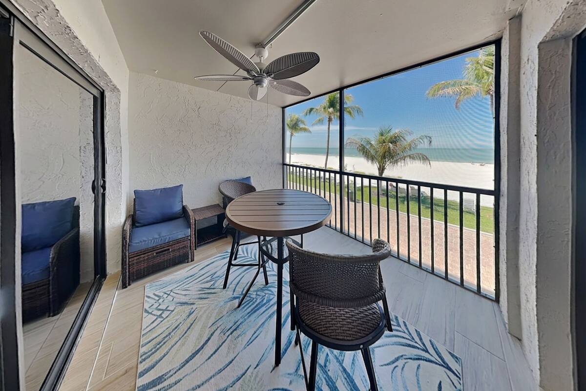 Un balcone con tavolo e sedie, una ventola a soffitto e vista sulla spiaggia.