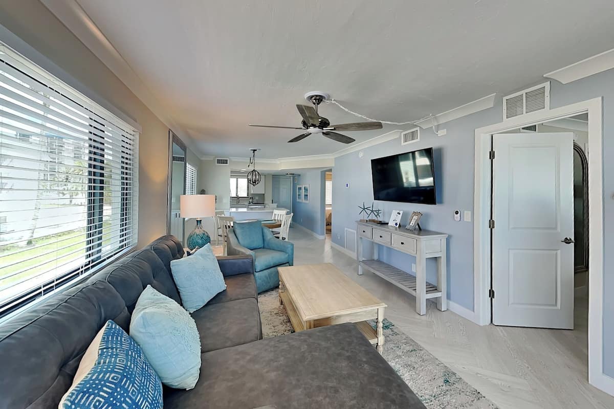 A modern living room with a grey sofa, blue cushions, a coffee table, and a TV on a stand.