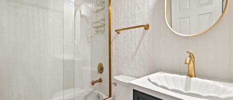 A modern bathroom with a glass-enclosed shower, a white bathtub, a white sink with a gold faucet, and a black vanity.