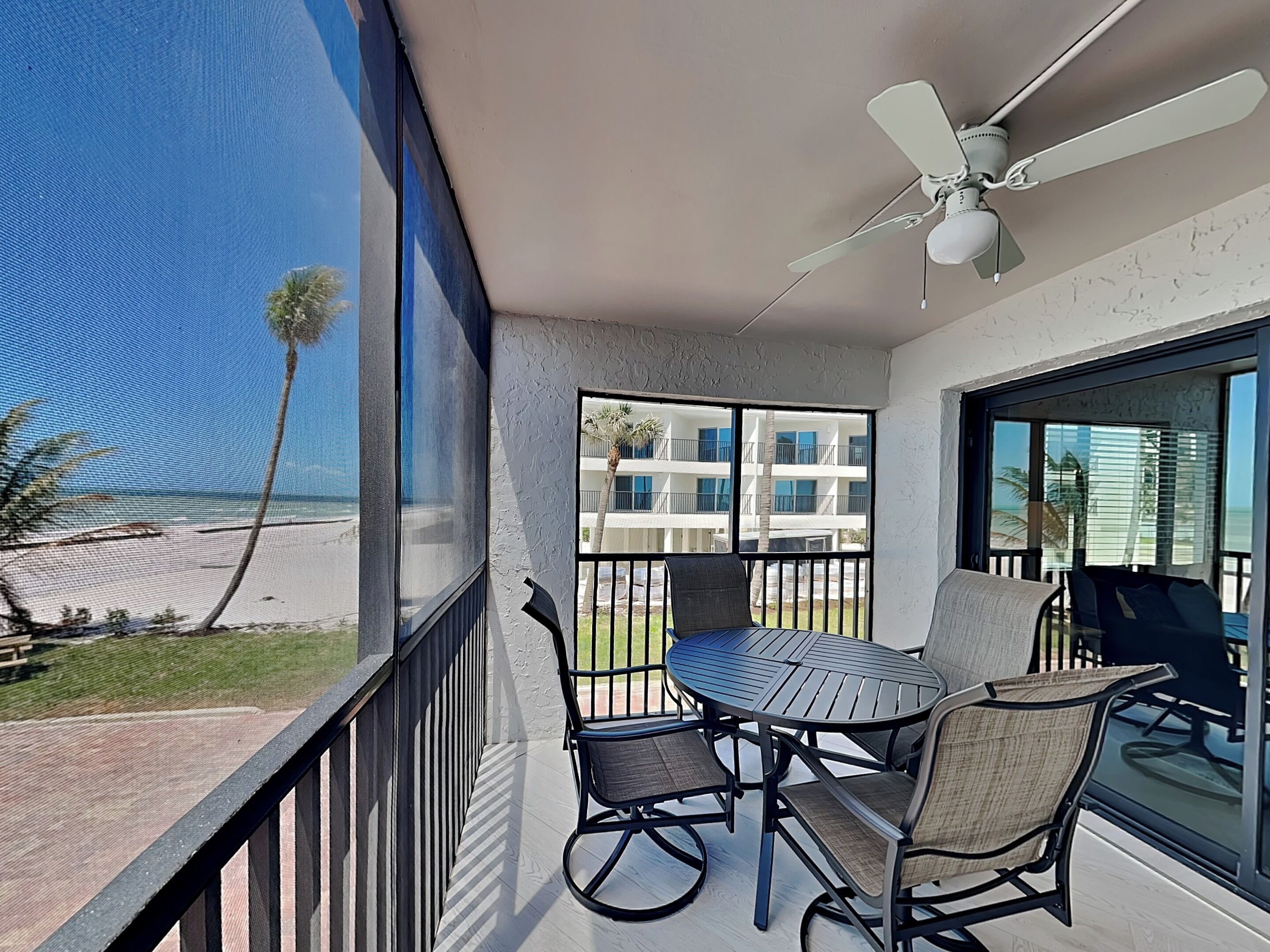 Un balcon avec une table et des chaises, un ventilateur de plafond et une vue sur la plage et les bâtiments.
