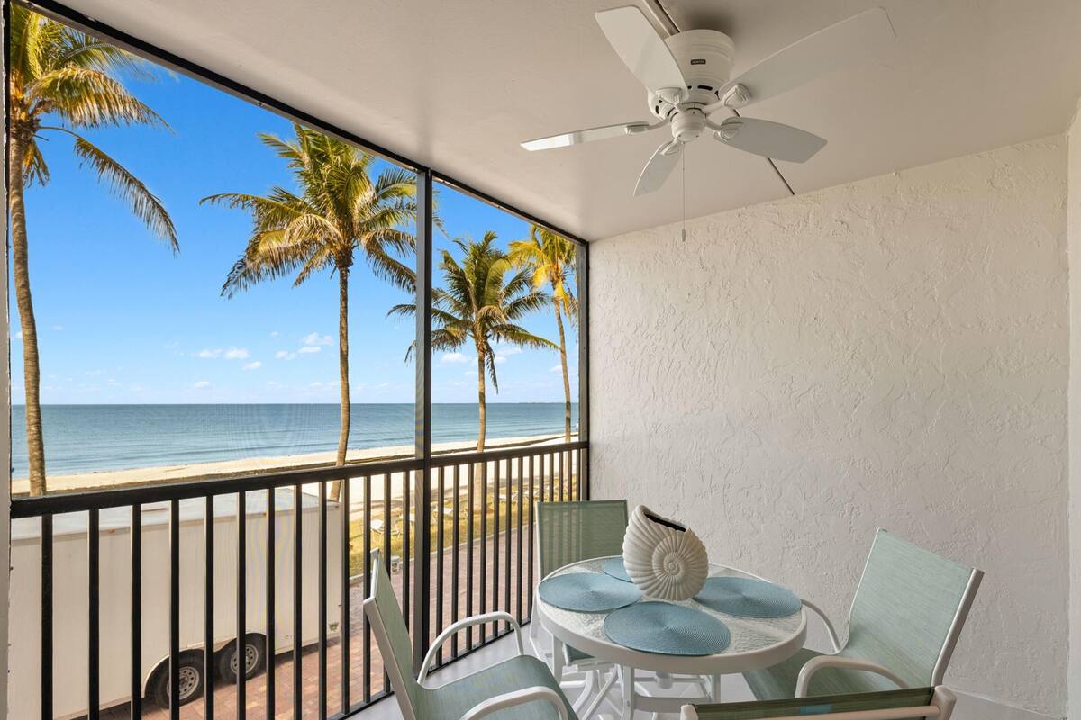 Un balcone con vista sulla spiaggia e sull'oceano, una ventola a soffitto e un tavolo con sedie.