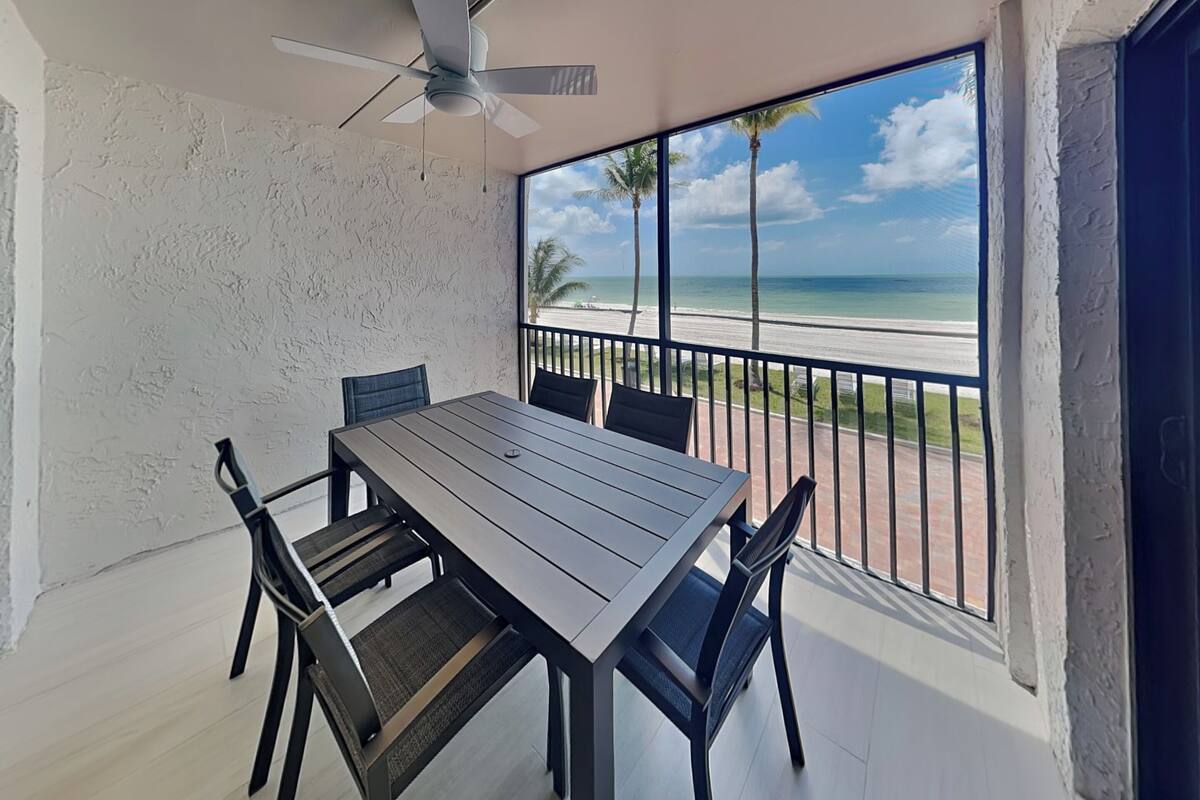 Un balcone con tavolo e sedie, una ventola a soffitto e vista sulla spiaggia.