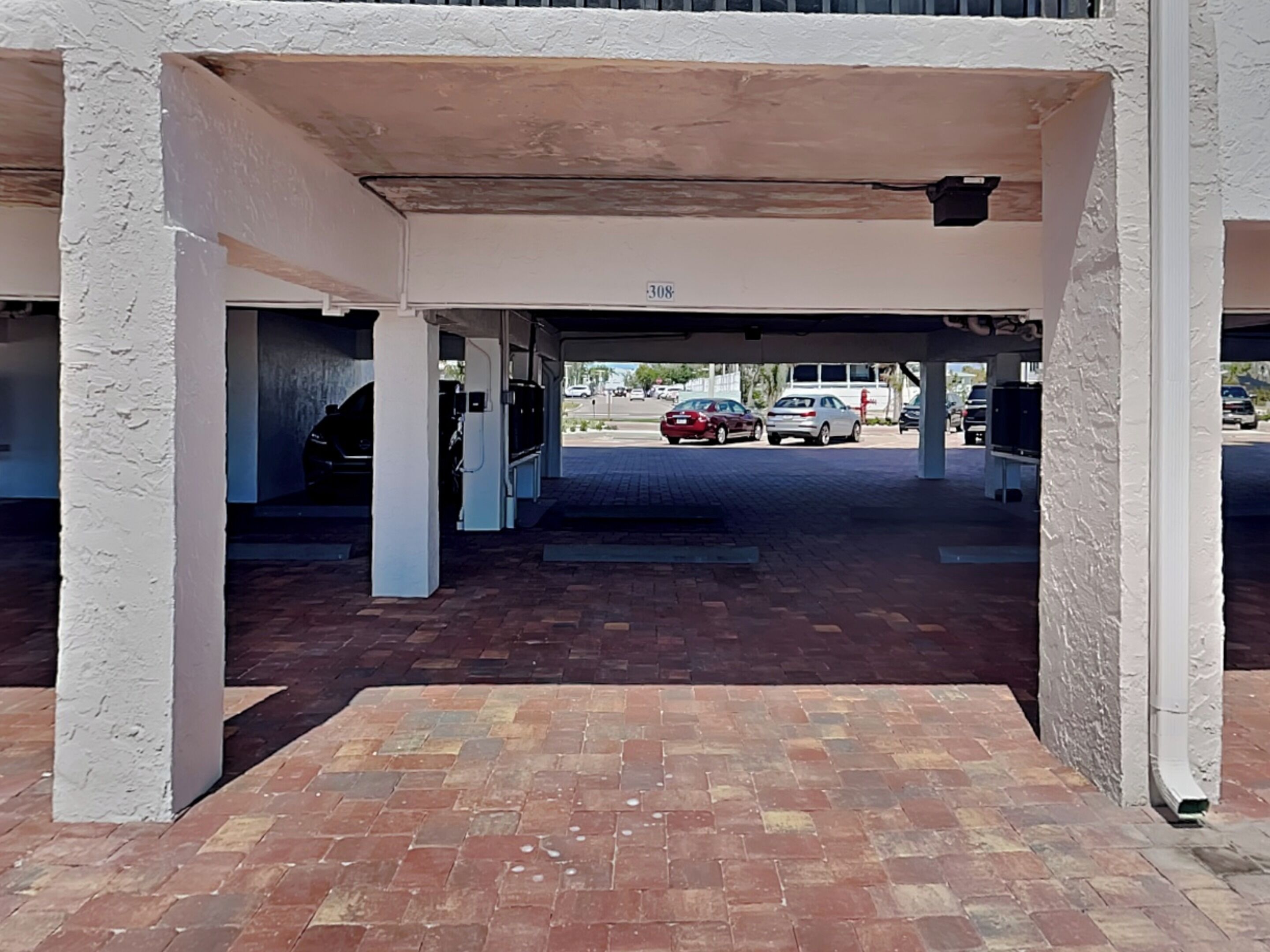 A covered parking area with a brick floor and a white wall with the number 308.