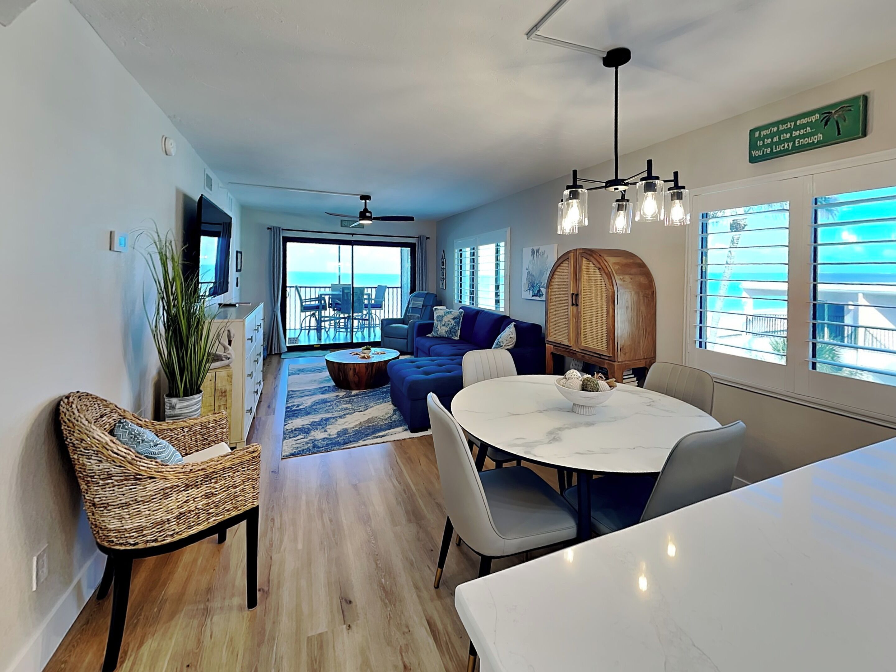 A modern living room with a sofa, dining table, and chairs. There is a large window with a view of the ocean.
