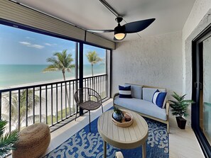 A balcony with a view of the beach, a sofa, a chair, a small table, and a potted plant. - Seaside 3 by Distinctive Beach Rentals (Fort Myers Beach)
