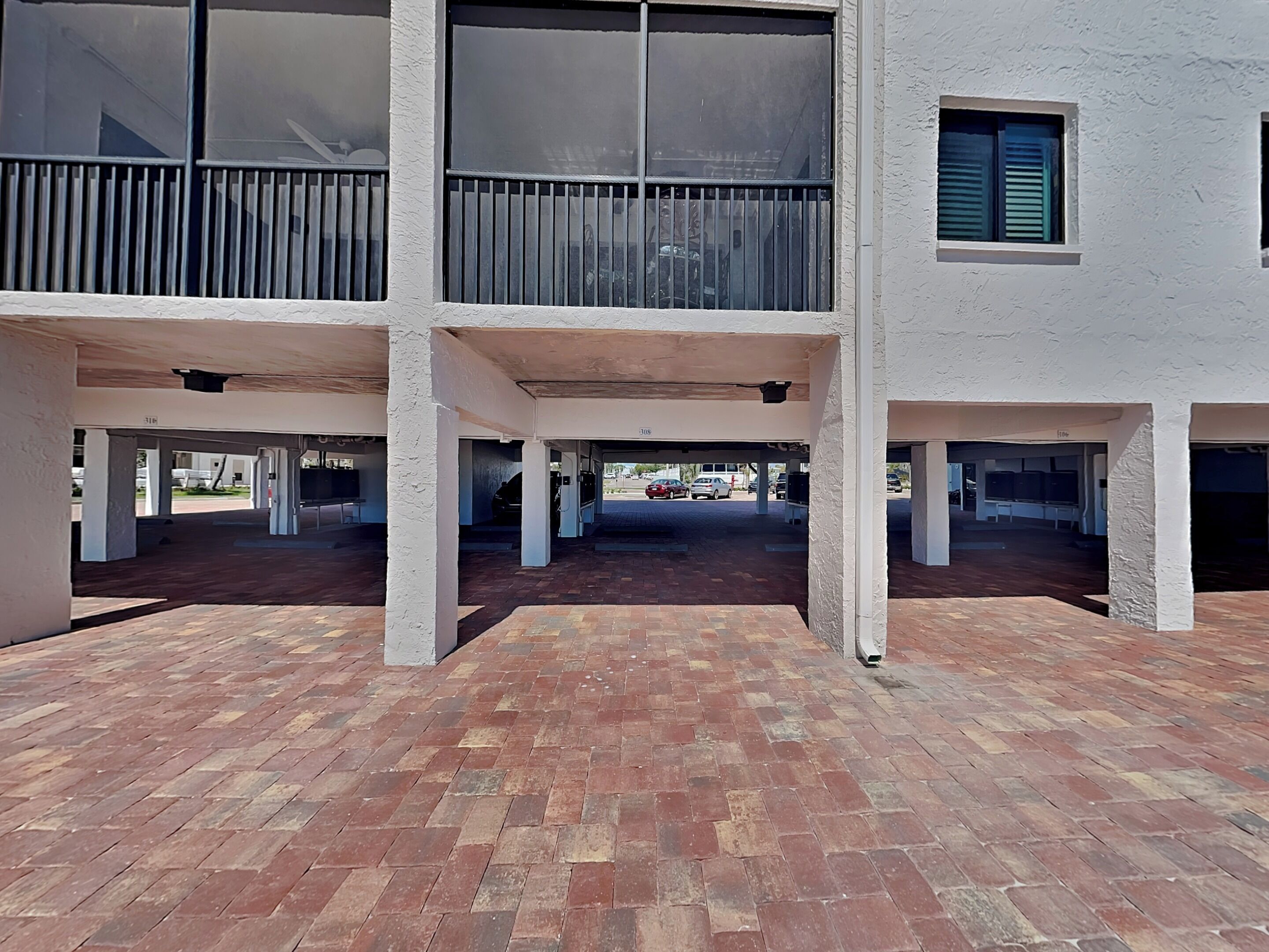 A covered parking area with multiple columns and a brick floor.