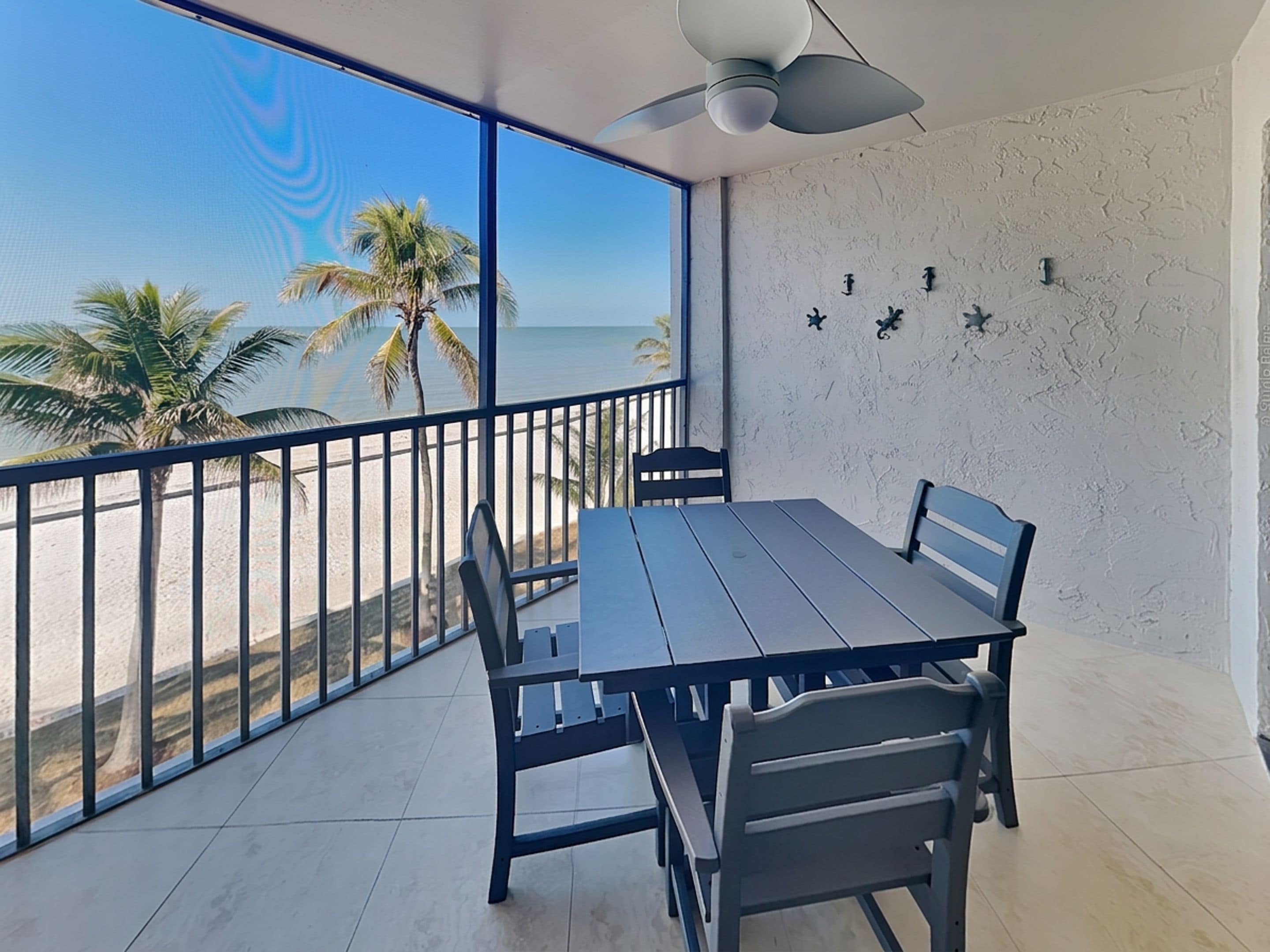 Un balcón con mesa y sillas, con vista a una playa con palmeras.