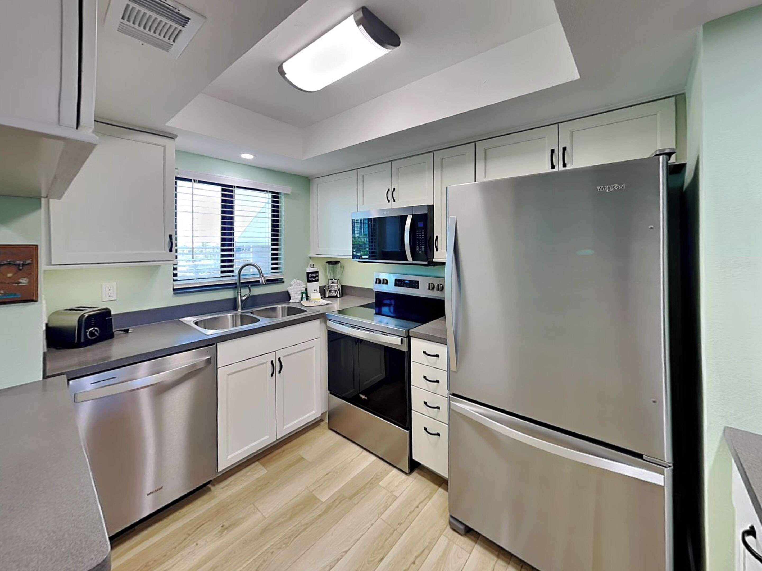 A modern kitchen with stainless steel appliances, a double sink, and light-colored cabinets.