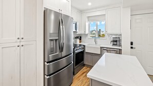 A modern kitchen with white cabinetry, stainless steel appliances, and a marble countertop. - Seaside 3 by Distinctive Beach Rentals (Fort Myers Beach)